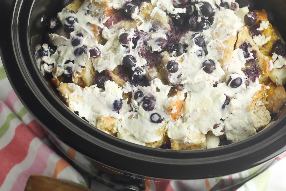 cream cheese spread over the top of the slow cooker breakfast casserole with blueberries.