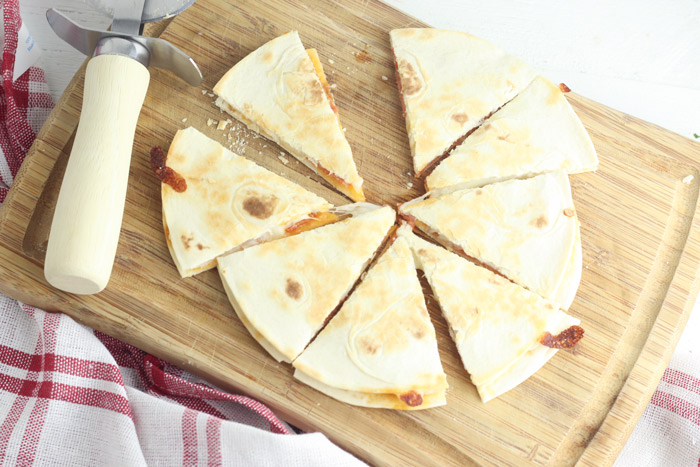 pepperoni and mozarella quesadilla cut into 8 slices on a wooden chopping board