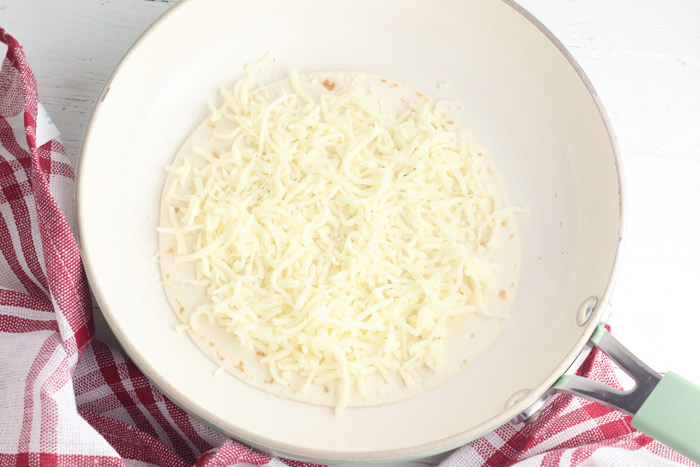 flour tortilla in a pan with shredded mozzarella on top