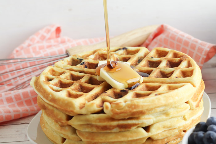 pouring maple syrup on a stack of blueberry waffles with butter on top
