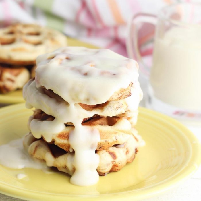 a stack of cinnamon roll waffles on a yellow plate drizzled with cream-cheese frosting