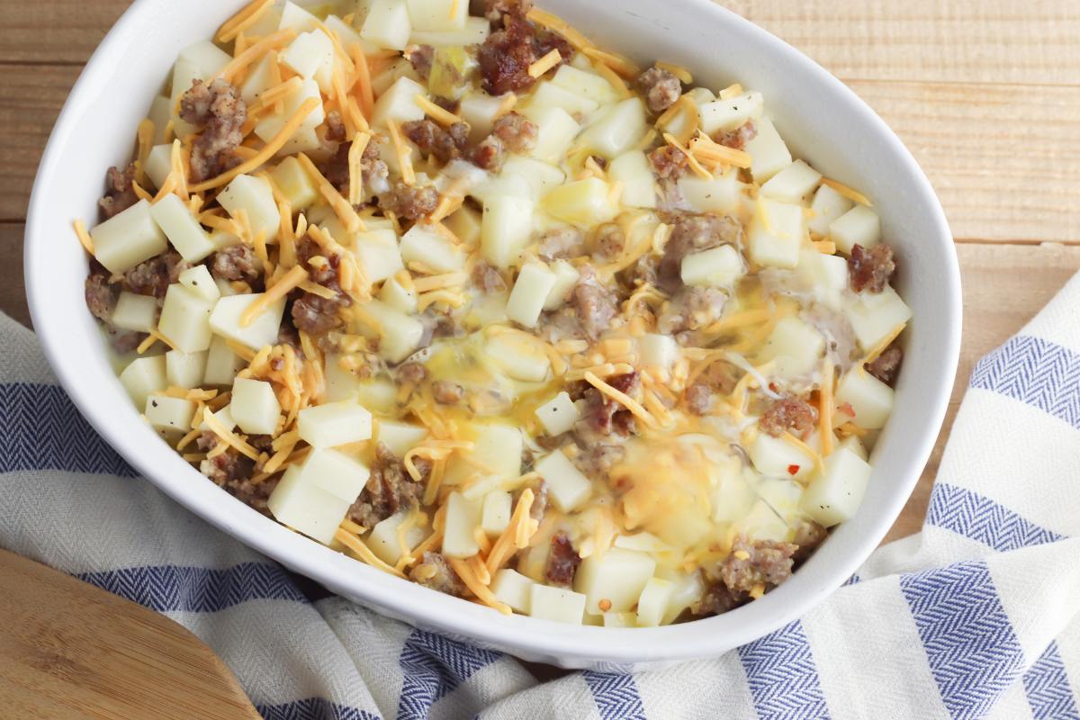 breakfast casserole making in a casserole dish egg mix poured over the sausage, potatoes and cheese mix.