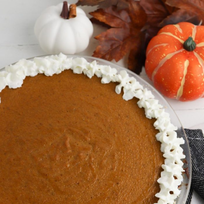 top down view of a simple homemade pumpkin pie on the table for thanksgiving with fall leaves and mini pumpkins and squash