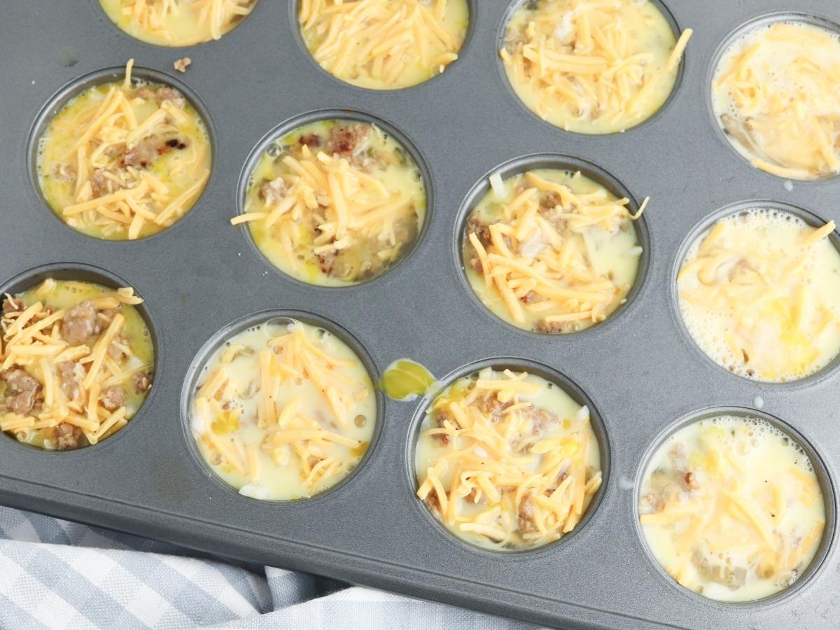 breakfast muffins ready to go in the oven with hash browns, sausage and cheese