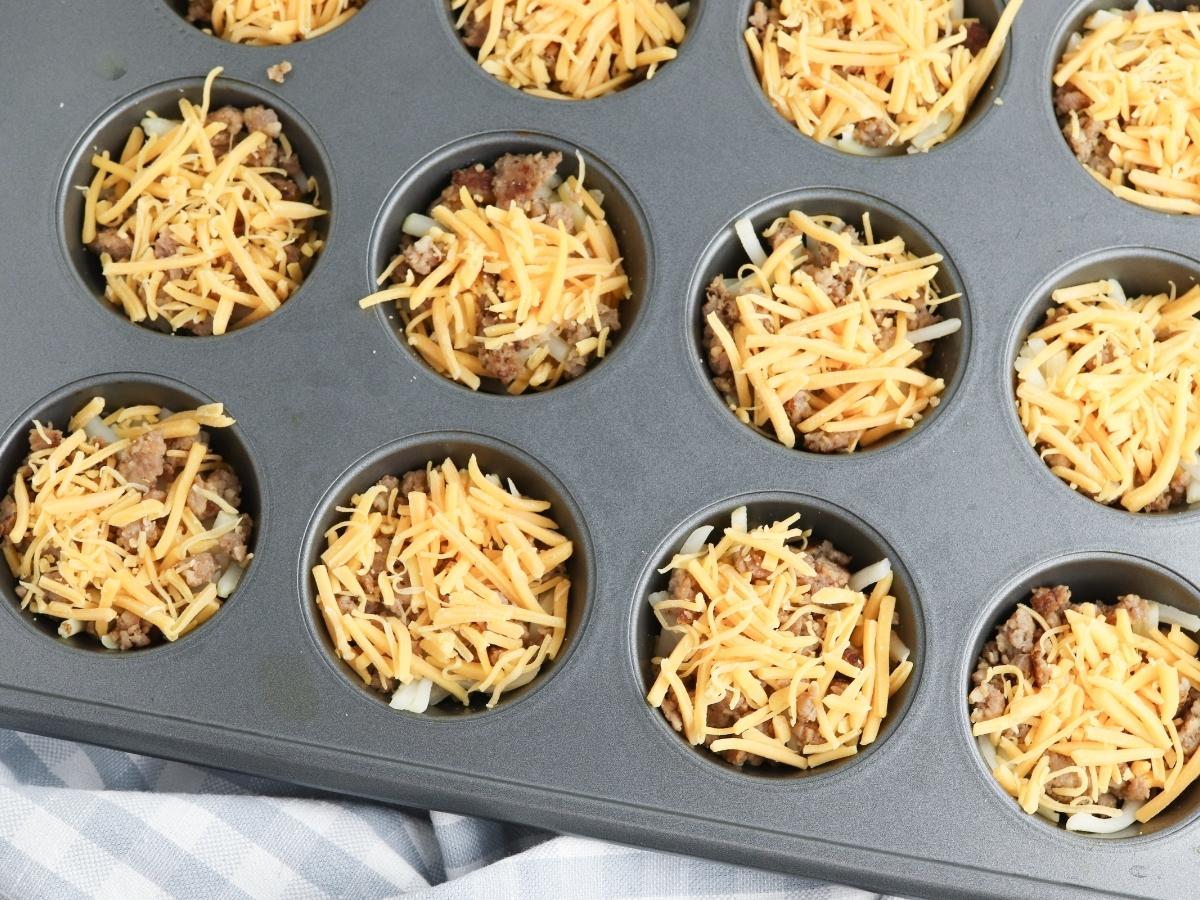 muffin tin with each cup filled with cheddar and breakfast sausage on top of hash browns
