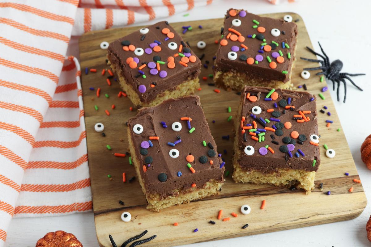 Top down view of 4 Halloween Cake Bars with chocolate frosting and sprinkles on a wooden chopping board.
