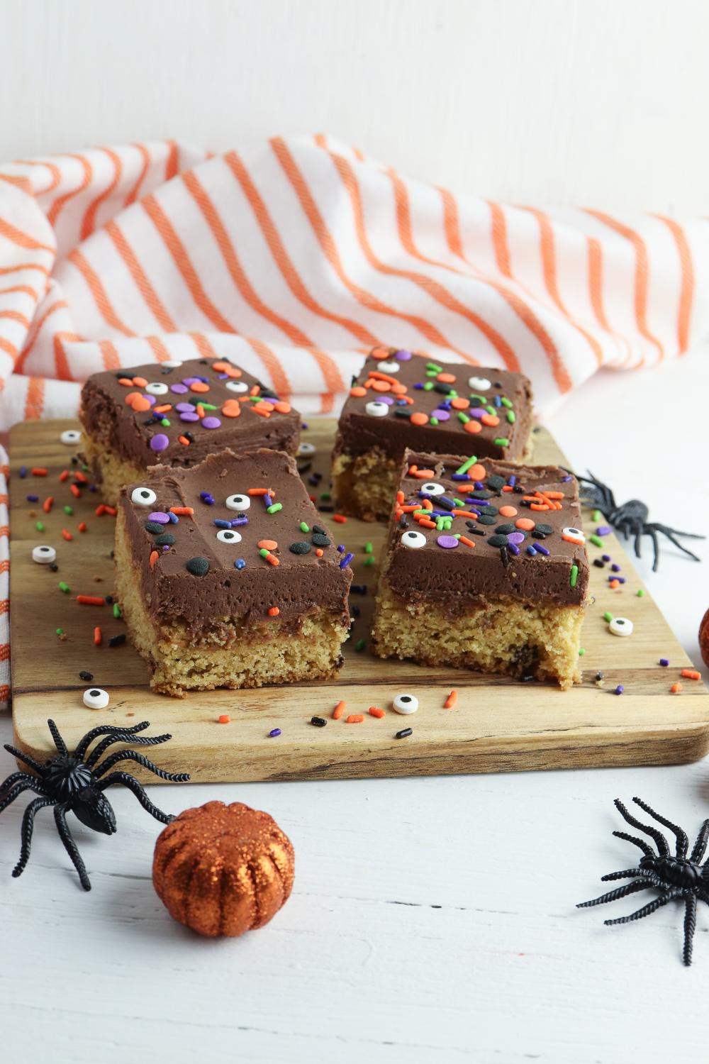 slices of Halloween Blondies on a wooden chopping board with Halloween themed objects around it.
