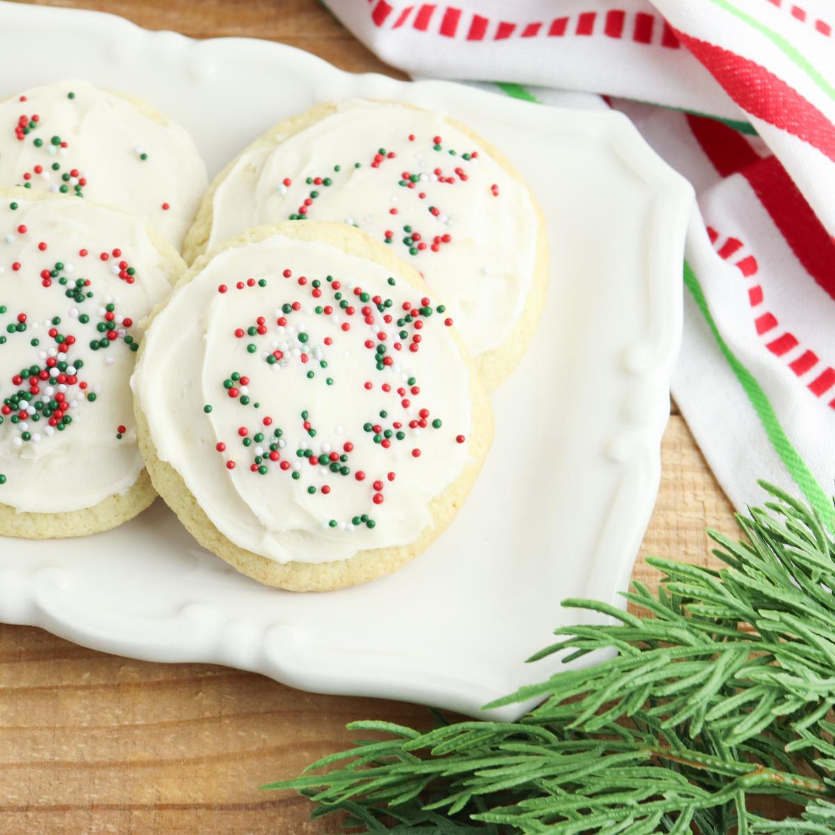 Simple Christmas frosted Sugar Cookies on a plate with cedar beside it.