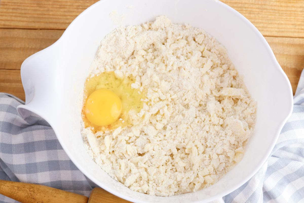 Egg added to the mixed butter and flour to combine to make a crust for the pecan pie.
