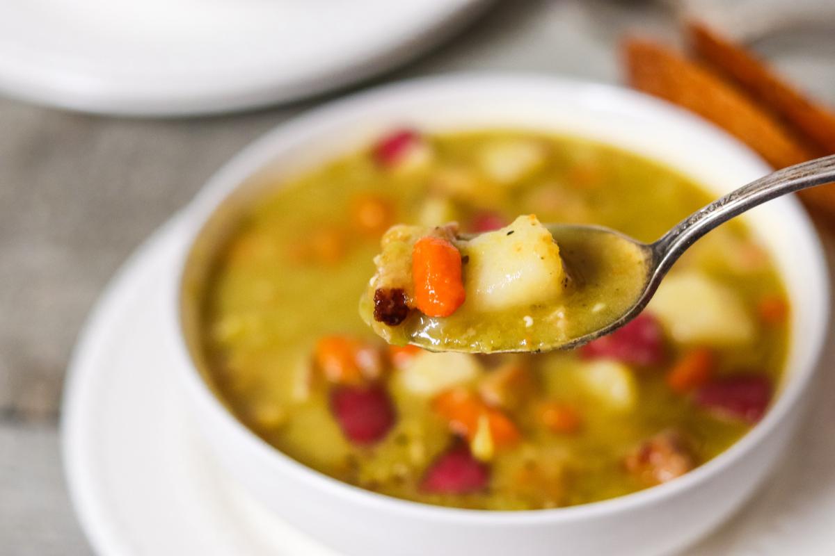 Delicious smoked pork, split pea and vegetable soup in a bowl with a portion on the spoon.