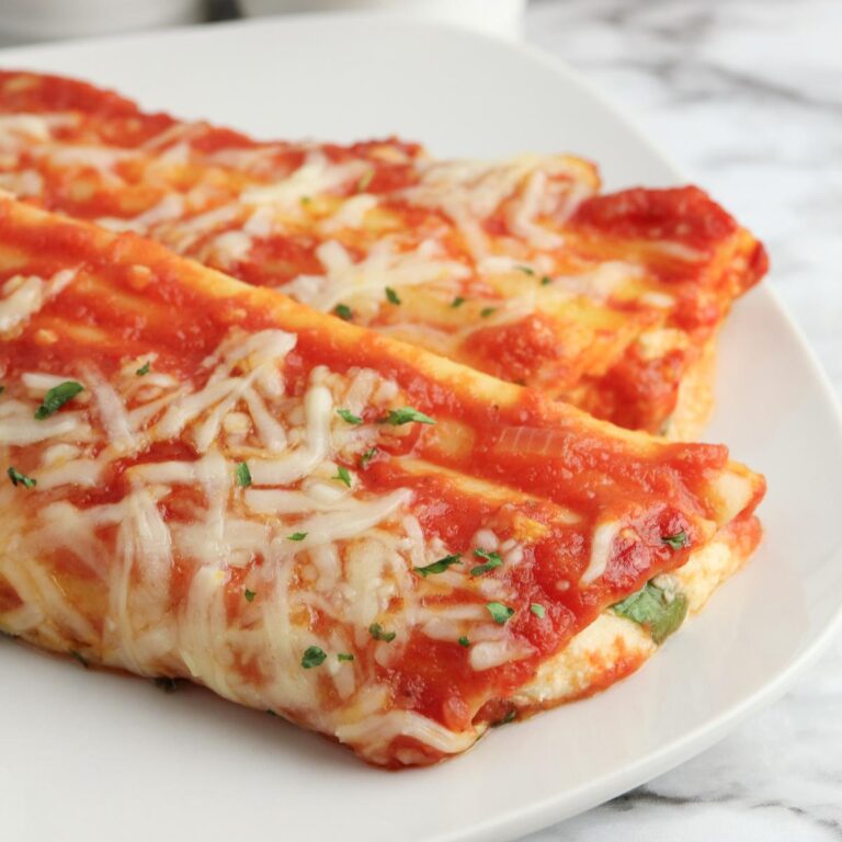 Close up of the cannelloni pasta tubes stuffed with spinach and ricotta cheese and baked with a simple homemade tomato sauce and melted cheese on a plate.
